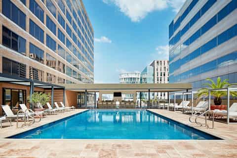 Luxury rooftop pool surrounded by high-rise buildings with lounge chairs and palm trees