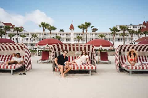 Beachfront cabanas with red and white striped canopies, hotel building with tower, and guests relaxing