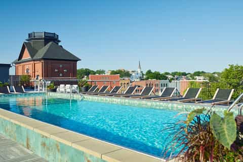 Rooftop pool with lounge chairs overlooking historic brick town buildings and church spire