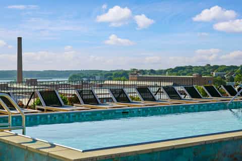 Rooftop pool overlooking river with lounge chairs and industrial chimney backdrop