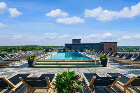 Rooftop pool with blue water, black and wood lounge chairs, cityscape and trees in background