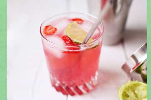 Pink strawberry cocktail with lime slice and ice in a glass with straw