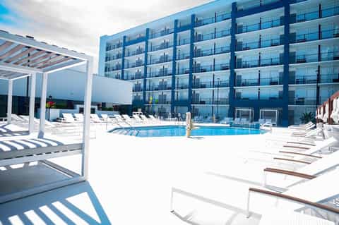 Contemporary resort pool with white loungers, pergolas, blue modern building, and clear sky