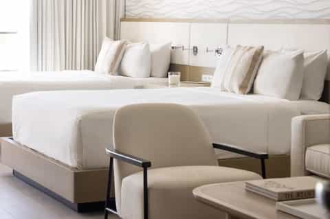 Luxury hotel suite with two queen beds, cream bedding, accent chair, and contemporary decor