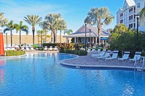 Resort pool surrounded by palm trees, lounge chairs, tropical vegetation, and white gazebo
