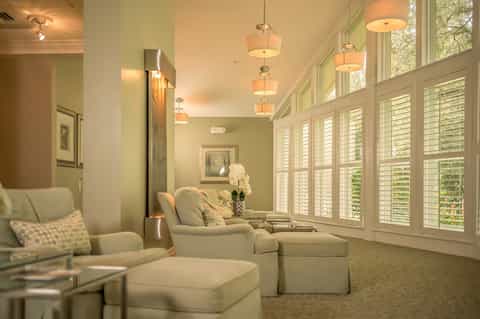 Wellness relaxation room with comfortable seating, green walls, pendant lighting, and large shuttered windows