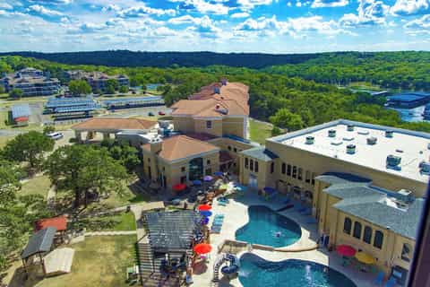 Aerial view of large resort complex with pools, buildings, landscaping, and surrounding forest landscape