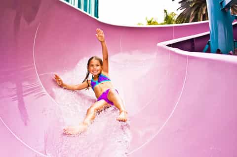 Child sliding down bright pink water slide at outdoor water park with splash of water