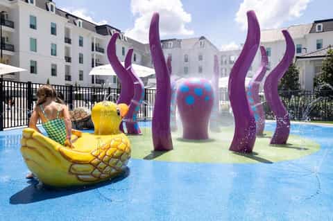 Children's pool area with colorful purple sculptural installations and splash pad features