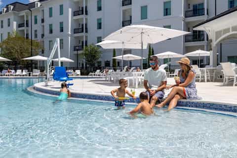 Family enjoying shallow pool area with white umbrellas and lounge chairs at resort