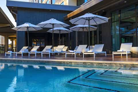 Contemporary resort pool with lap lane, lounge chairs, blue umbrellas, and modern building