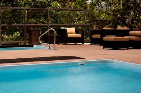 Two resort pools on terrace with lounge seating, black furniture, and landscaped vegetation backdrop