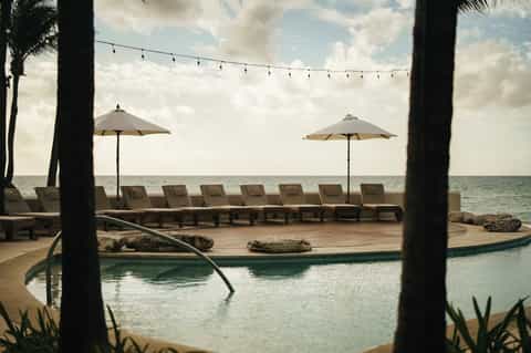 Beachfront infinity pool overlooking ocean with lounge chairs and umbrellas
