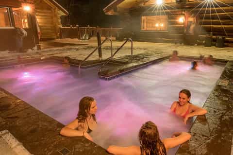 Outdoor hot spring pools with pink lighting at night, surrounded by wooden buildings