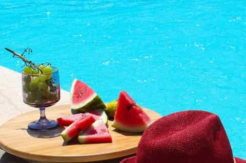 Poolside refreshment with cocktail and watermelon slices on wooden deck by turquoise water