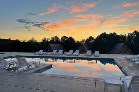 Resort swimming pool at sunset with lounge chairs, cabanas, and colorful sky reflection in water