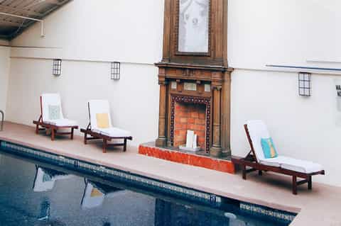 Indoor lap pool with wooden lounge chairs on deck, decorative fireplace, and industrial ceiling