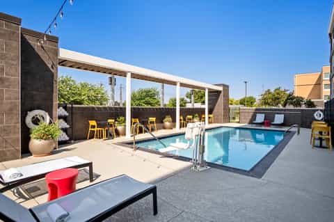 Rooftop pool deck with blue swimming pool, loungers, pergola, and yellow accent chairs