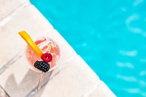Tropical cocktail with fruit garnish on poolside lounge chair by turquoise water