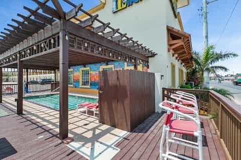 Covered pool area with pergola, red lounge chairs, and wooden pavilion structures
