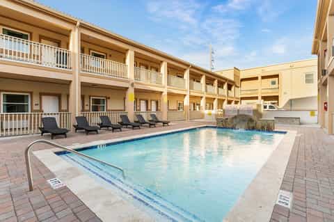 Indoor hotel pool with turquoise water, black loungers, and multi-level building