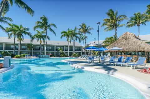 Large lagoon-style pool with palms, tiki umbrellas, lounge chairs, tropical resort setting
