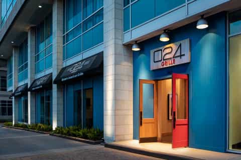 Modern restaurant storefront with blue exterior, orange door, and neon signage