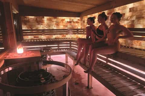 Spa sauna with warm wood tones, bench seating, and three people relaxing inside
