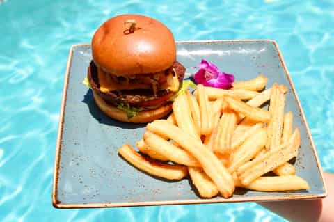 Gourmet burger and french fries on plate floating in resort pool under sunlight