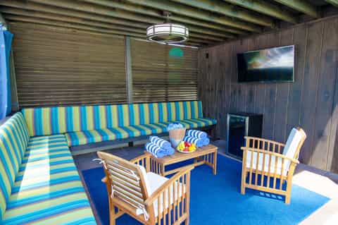 Covered patio lounge area with striped sofa, wooden chairs, and entertainment system
