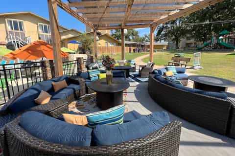 Outdoor patio with curved rattan seating, fire pit table, wooden pergola, and orange umbrella