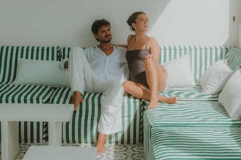 Couple sitting on green and white striped bed in minimalist hotel room with white walls