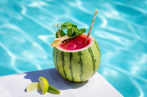 Tropical cocktail served in hollowed watermelon with mint and straw by swimming pool