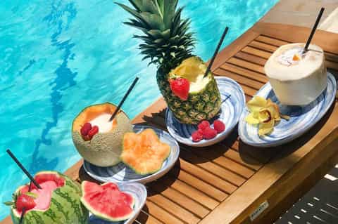 Tropical poolside cocktails with pineapple, melon, and coconut drinks on wooden deck