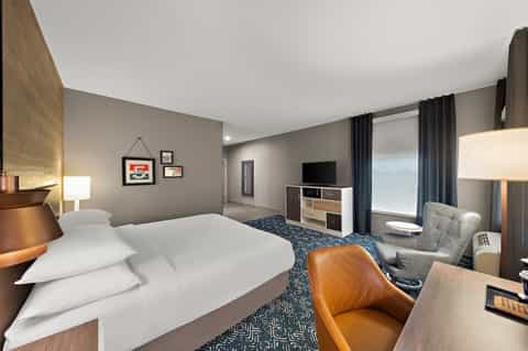 Spacious hotel bedroom with queen bed, flat-screen TV, and contemporary furnishings