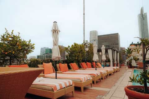 Urban rooftop lounge with orange striped loungers, white umbrellas, and city skyline