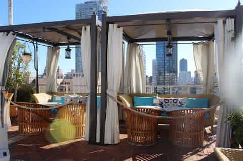 Rooftop lounge with wooden chairs, white curtains, and city skyline views