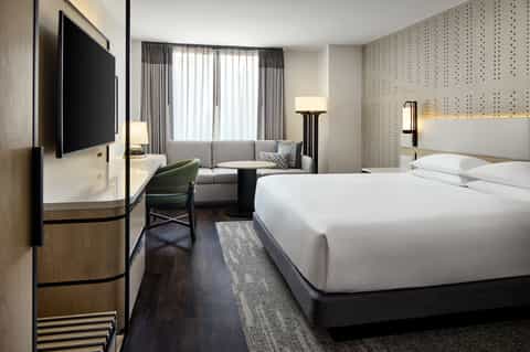 Modern hotel bedroom with king bed, contemporary furnishings, flat-screen TV, and sitting area
