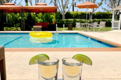 Two shot glasses with lime wedges by pool at resort with yellow float and lounge chairs