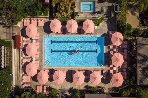 Aerial view of resort pool surrounded by pink umbrellas, lounge chairs, and manicured grounds