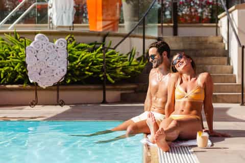 Couple relaxing poolside at modern resort with decorative towel arrangement and city views