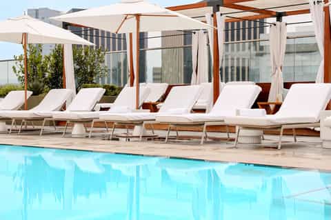 Resort pool deck with white loungers, umbrellas, pergolas, and high-rise buildings in background