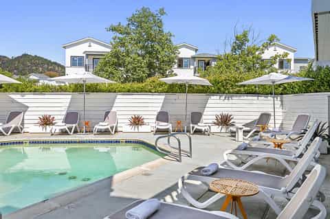 Resort pool surrounded by white loungers, umbrellas, and modern white buildings