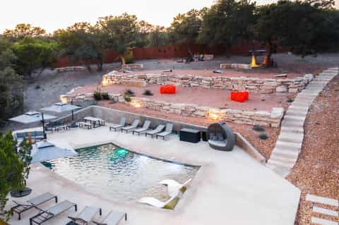 Desert resort with infinity pool, lounge chairs, fire pit, stone amphitheater, and native desert landscaping