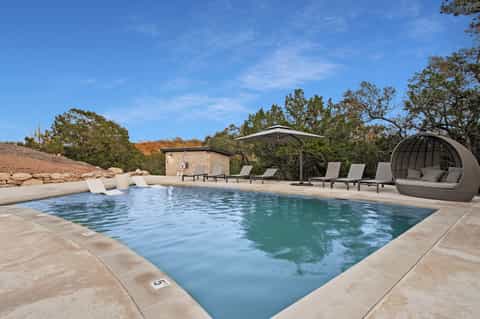 Desert resort pool with loungers, cabana pod, stone structure, and scenic rock formations