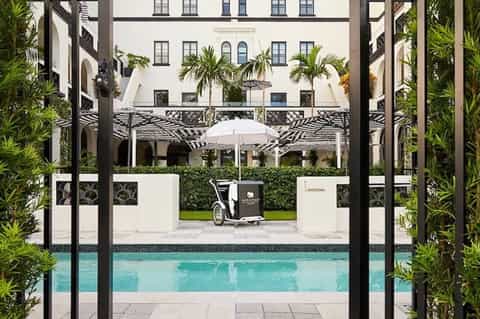 Elegant courtyard pool with white umbrellas, tropical plants, and classical building facade