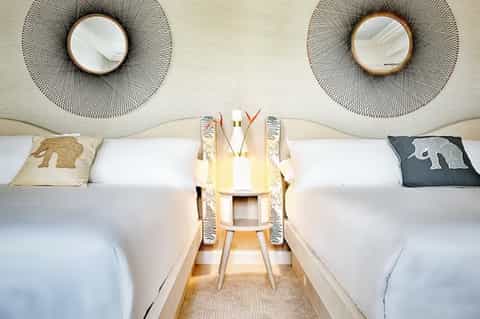 Contemporary hotel room with twin beds and decorative woven mirrors above headboards