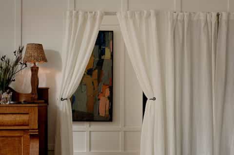 Elegant entryway with cream curtains framing doorway and wooden side table with lamp