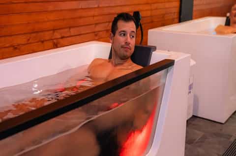 Man soaking in luxurious spa tub with red ambient lighting and wooden interior finish