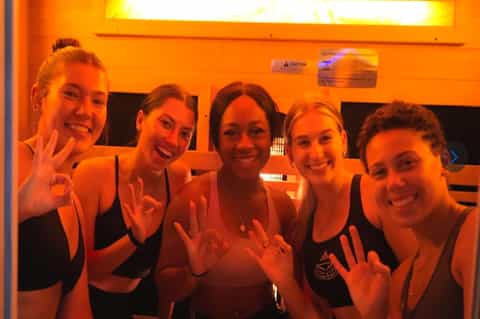 Five women in sports attire smiling in infrared sauna room